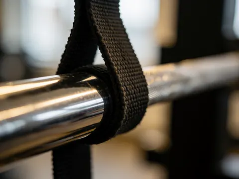 Black fitness strap tied to a chrome weight bar in a gym with metallic reflections and a blurred background