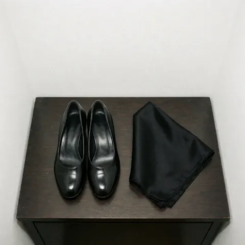 Black tango shoes and a silk scarf arranged on a dark wooden surface for tango business use