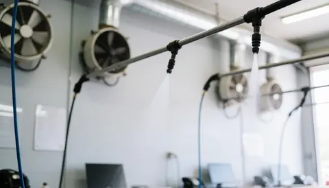 Water booms and industrial fans mounted on gray walls in a clean car wash with diffused lighting, providing a professional background for text.