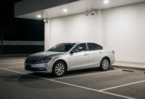Silver sedan parked in a well-lit covered parking garage with security cameras, suitable for ride-hailing drivers.