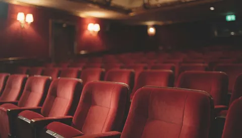 Empty red velvet theater seats illuminated by warm lights, suitable as a background for event and venue rental text overlays