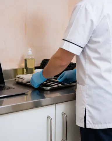 A therapist wearing blue gloves arranges massage tools on a metal tray placed on a stainless steel table in a clinical setting.