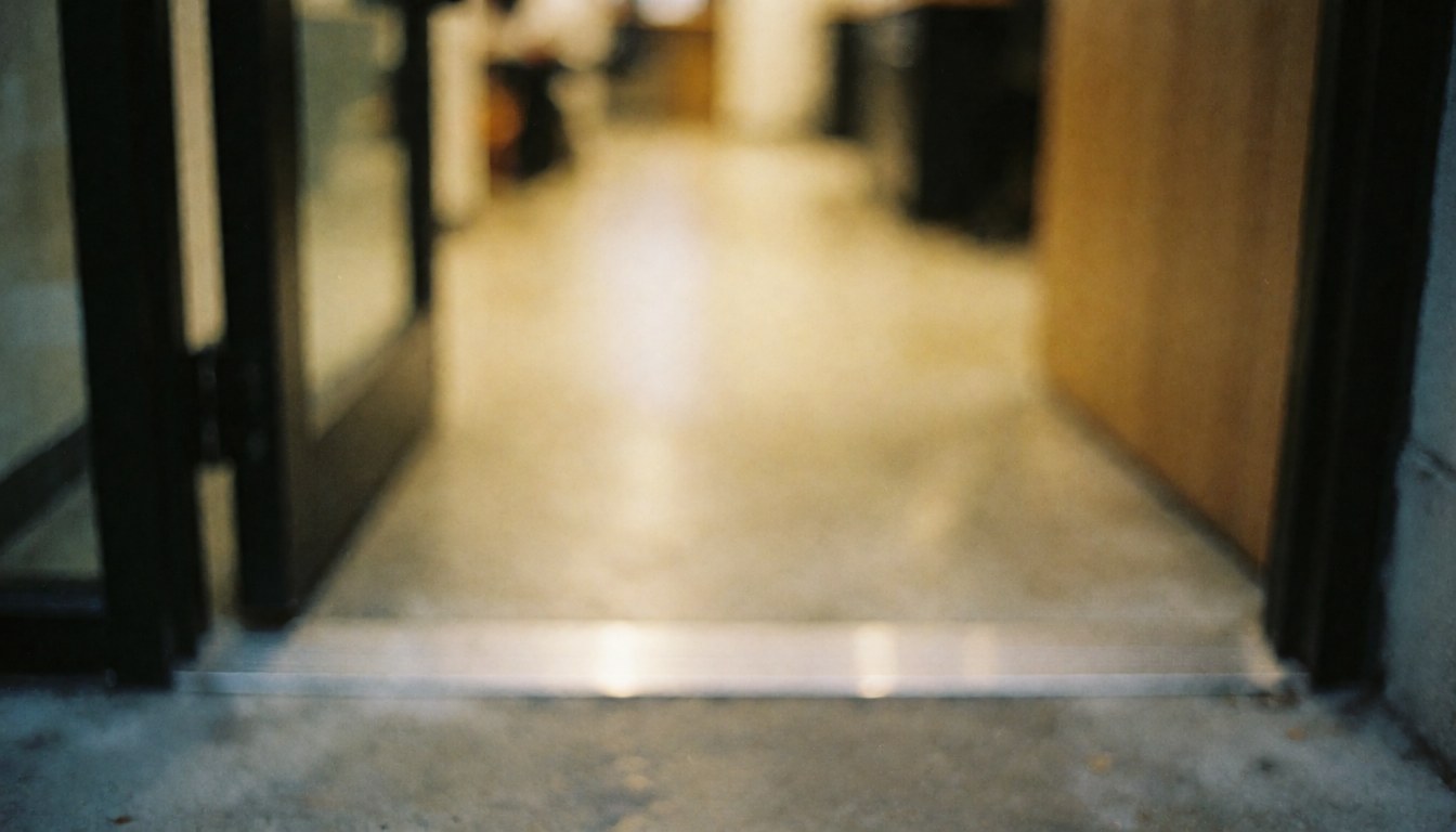 Close-up of a metal door threshold installed on a door frame with a blurred interior floor and warm lighting, suitable for text overlay.