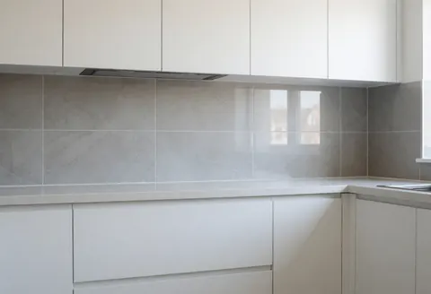 Modern kitchen featuring newly installed gray ceramic tiles, white cabinetry, and a window letting in natural light.