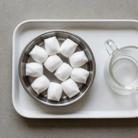 Wet cotton swabs in a metal container on a white tray next to a glass, prepared for cupping massage treatment