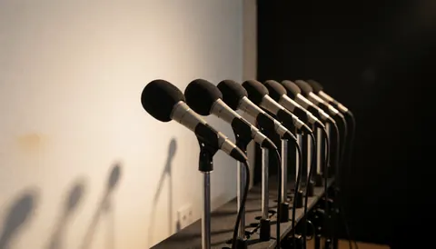 Dynamic microphones mounted on metal stands ready for events, set against a white wall with warm lighting for professional sound.