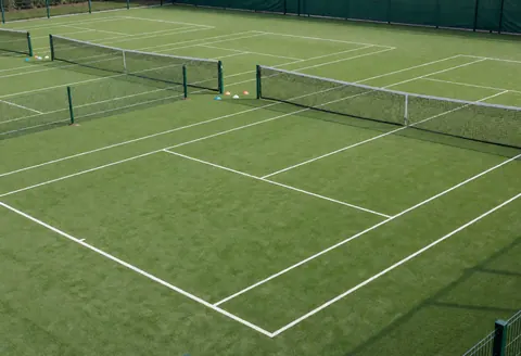 Three outdoor tennis courts with green synthetic surfaces, white boundary lines, and nets, ideal for tennis training.