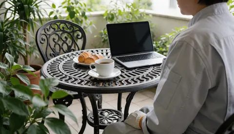 Person working on a wrought iron table with laptop, coffee, and pastries, ideal for a bed and breakfast
