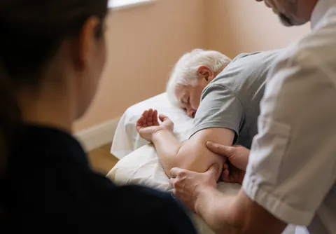 Therapist performing sports massage on a client's arm while lying on a table in a relaxed beige room