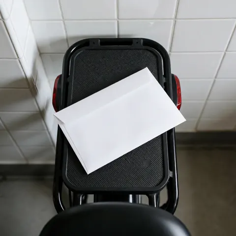 A white container placed on the rear rack of a bicycle against a background of white tiled walls with natural lighting.