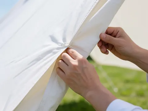 Close-up of hands adjusting white tent fabric on green grass under natural light, suitable for event furniture rental details.