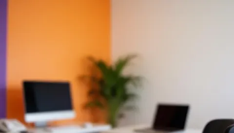 Office background featuring orange and purple walls, a computer, laptop, and plant, ideal for text overlays