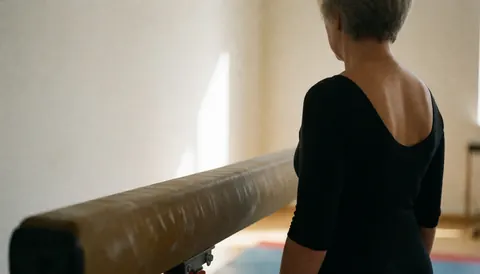 Gymnastics coach standing next to a balance beam in a gym with white walls and natural light