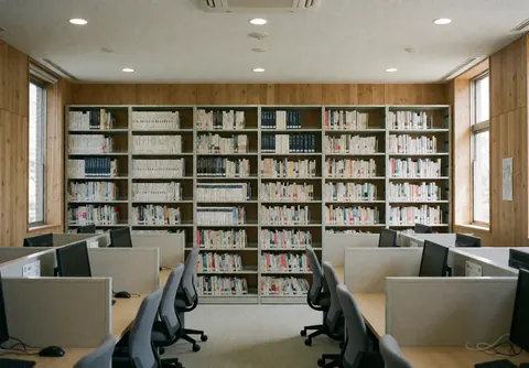Technical library featuring metal shelves filled with books, study carts, ergonomic chairs, wooden walls, and natural light.