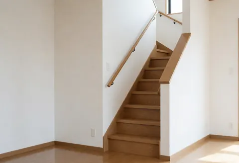 Close-up of a newly installed wooden staircase with a railing, white walls, and light wood flooring in a residential interior