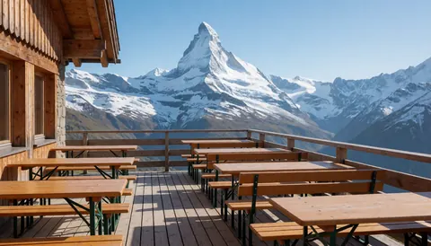 Wooden terrace with tables and benches offering panoramic views of snow-covered mountains at a winter mountain hut.