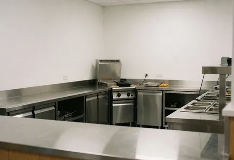 Professional kitchen featuring an industrial stove, stainless steel tables, and white walls suitable for a fun center.