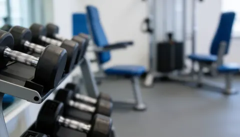 A neutral background featuring dumbbells and gym training machines, suitable for text overlays about physical preparation and recovery.