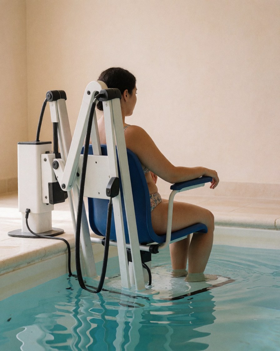 A person using a hydrojet chair in a swimming pool with beige walls, suitable for swimming coaches.