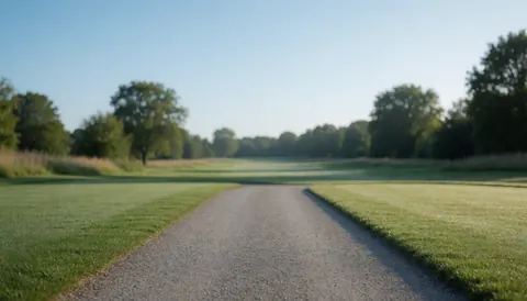 A gravel path winds through a well-manicured golf course with green grass, trees in the background, and a clear blue sky, ideal for text overlay.