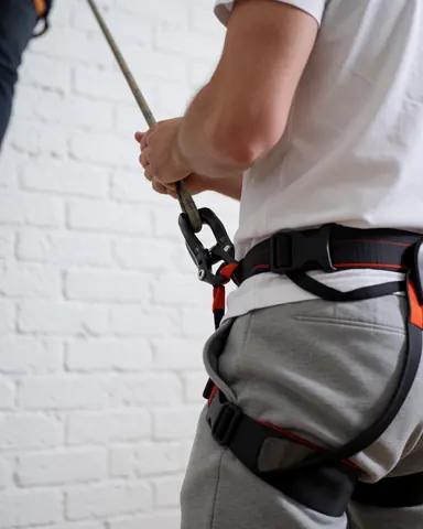 Close-up of belayer using rope and harness on white brick wall for climbing class safety equipment display