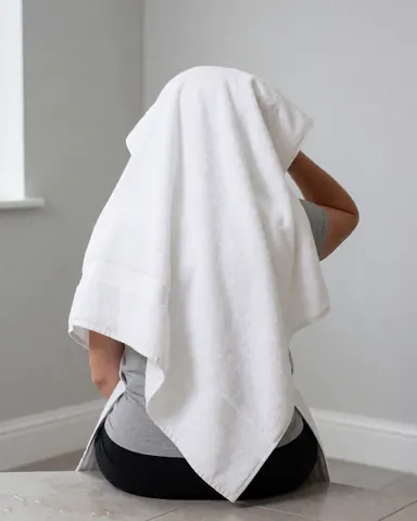 Person drying hair with white towel sitting on tiled floor with light gray walls, suitable for vacation rental context