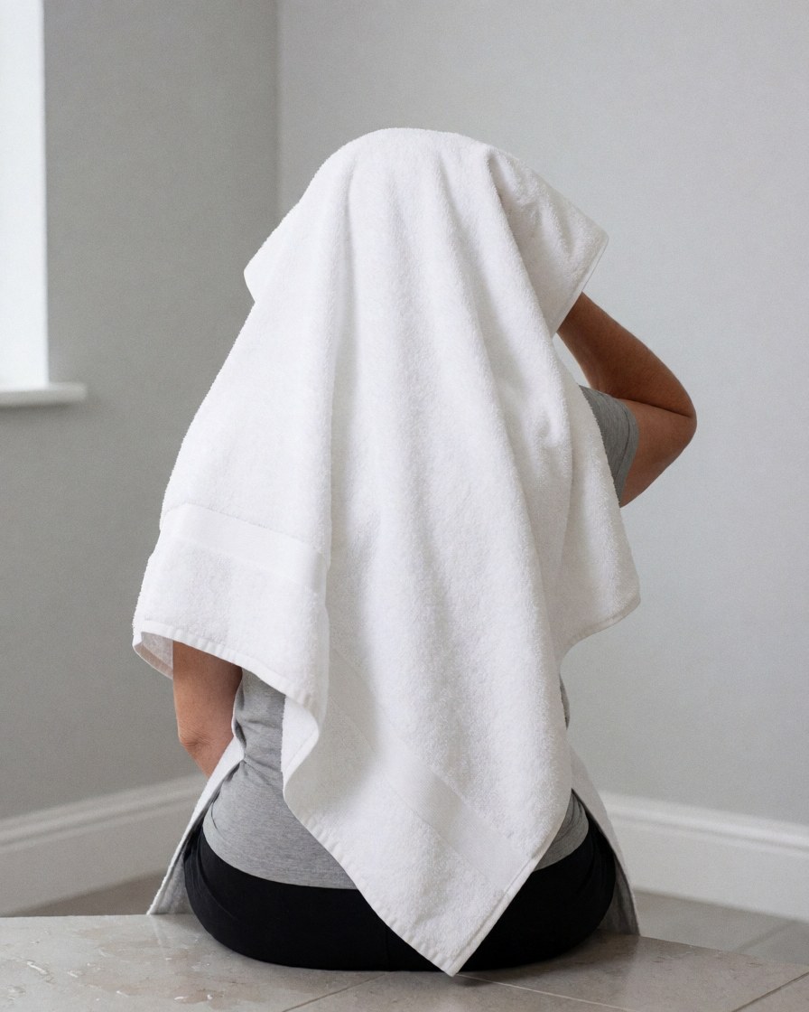 Person drying hair with white towel sitting on tiled floor with light gray walls, suitable for vacation rental context