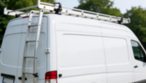 White work van equipped with ladder racks on the roof, set against a background of green trees, suitable for window installation text overlays.