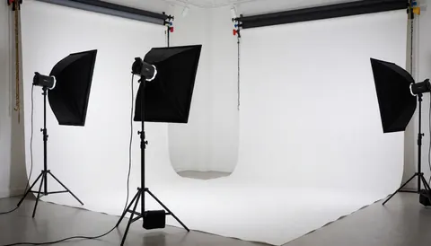Professional photo studio with white background and three lighting stands ready for portrait sessions