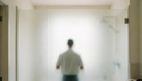 Glass installer placing an opaque glass panel in a modern bathroom with warm white walls and diffused light