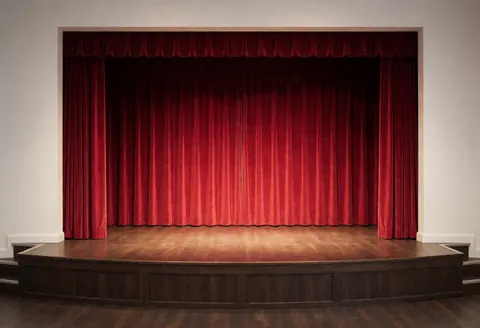 An empty dance stage featuring a polished wooden floor and draped red curtains, suitable for recitals and professional events.
