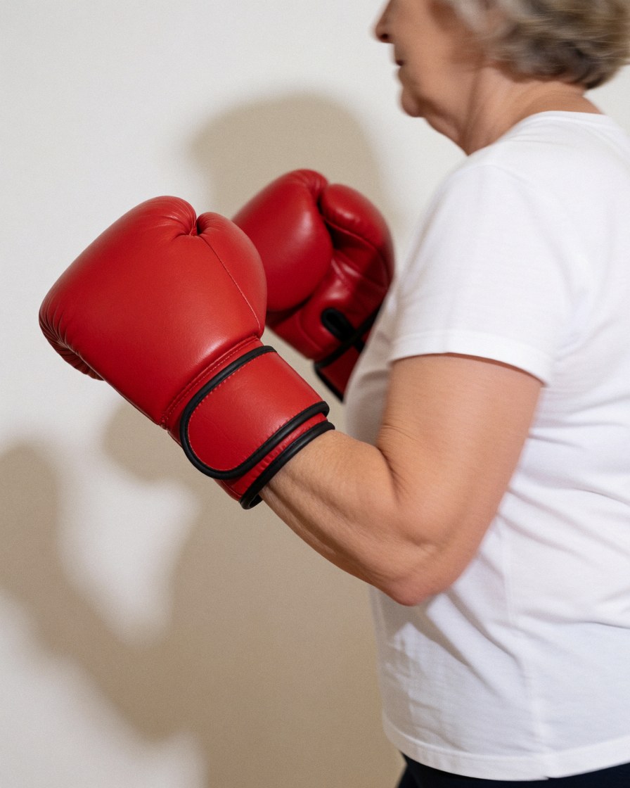 Senior woman in motion wearing red boxing gloves against a white wall, suitable for women's self-defense or gym training contexts