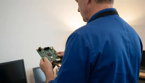Technician inspecting a circuit board in a workshop with a white wall and warm lighting for tv repair