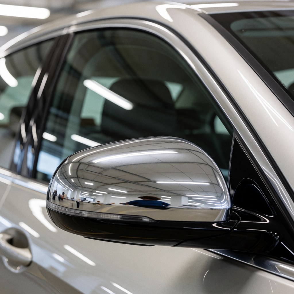 Close-up of a chrome rearview mirror and clean window of a white car parked in a garage with fluorescent lighting.