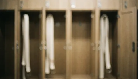 White karate belts hanging on wooden lockers in a dojo locker room with warm lighting, suitable as a background for text.