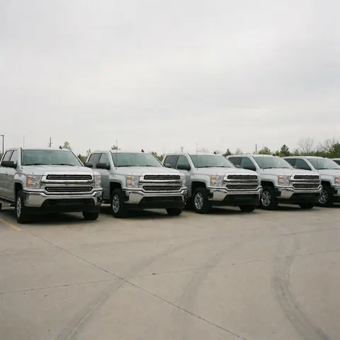 Wide view of a row of silver pickup trucks in a concrete lot under a cloudy sky, ideal for vehicle sales.