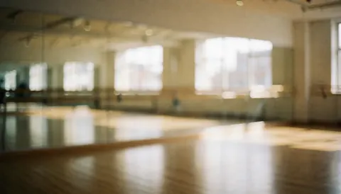 Empty dance studio interior featuring wall mirrors, wooden flooring, and natural light, providing a clean background for text overlay