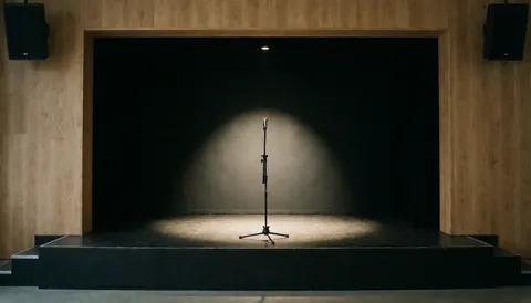 A microphone on a stage under a spotlight, with wooden walls and a black background, ideal for a website cover.