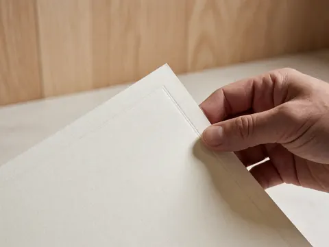 Close-up of a hand holding a white diploma with an embossed border on a light wooden surface with soft lighting