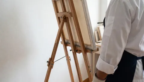 Easel holding a blank canvas in a studio with white walls, viewed from behind, ideal for art courses
