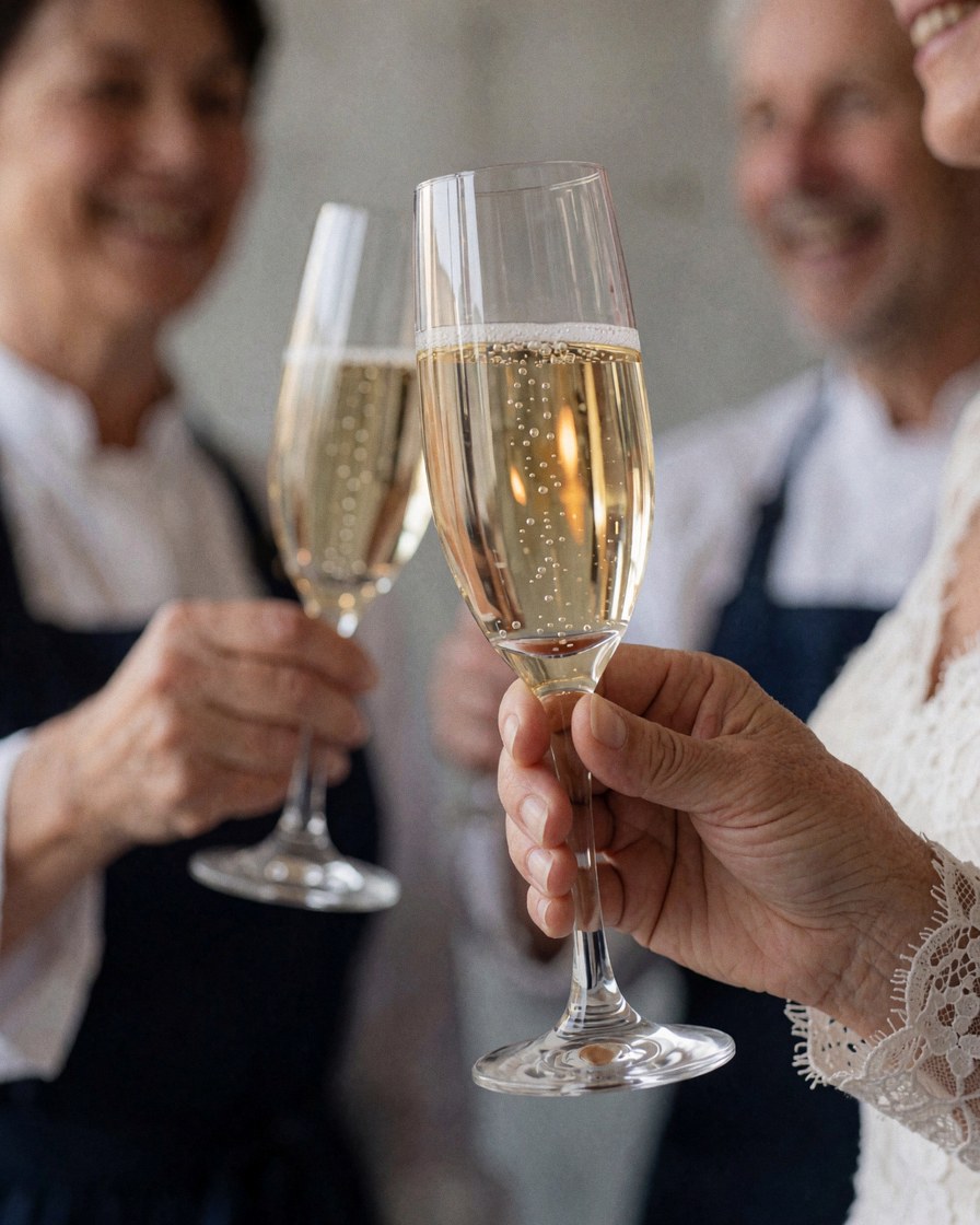 Close-up of a woman's hand in a lace sleeve holding a champagne glass with bubbles during a wedding toast