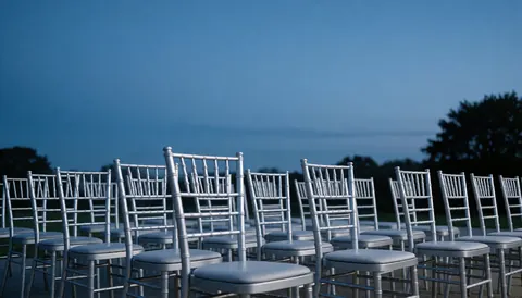 Rows of metal Chiavari chairs set up outdoors under a blue sky, ideal for weddings or formal galas.