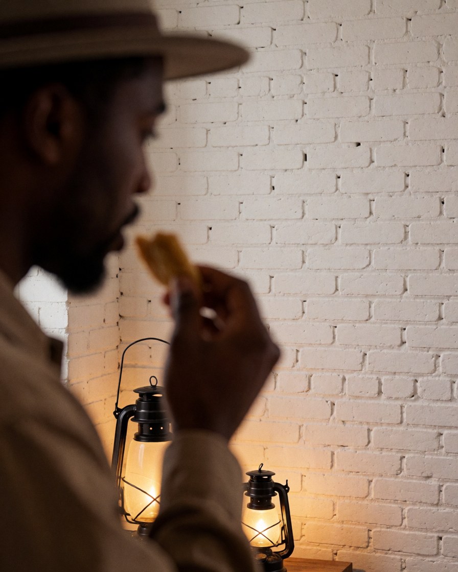 A man enjoys traditional food at a night festival illuminated by lanterns with a white brick wall background.