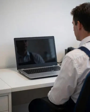 A technician working on a laptop in a clean, professional office with soft lighting and white walls.