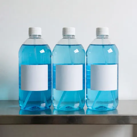 Three empty blue disinfectant bottles with white labels arranged on a metal shelf for cleaning or hygiene business use