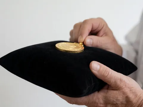 Close-up of adult hands holding a gold medal on a black velvet cushion against a white background