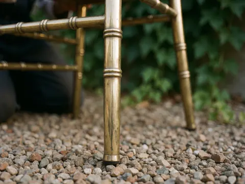 Close-up of bronze chair legs on gravel with green leaves and golden light reflections for event furniture rental