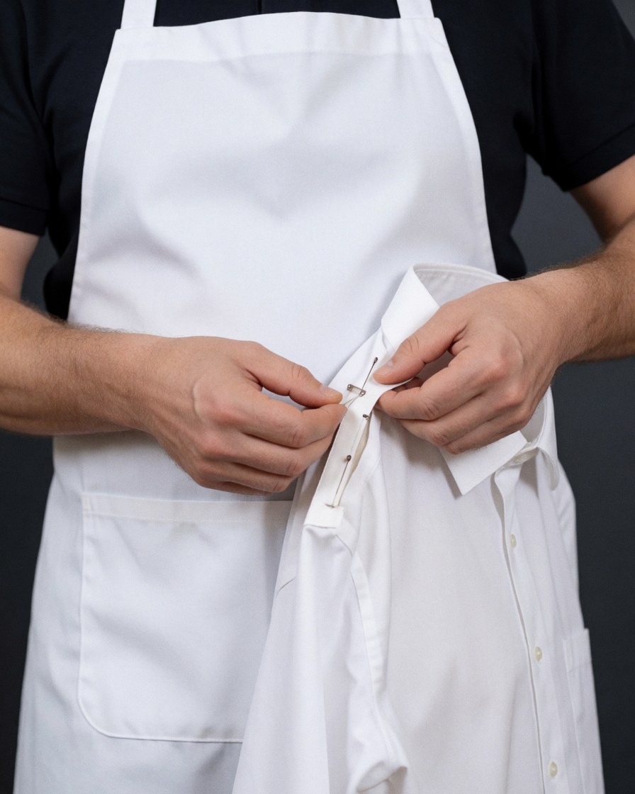 Hands pinning the collar of a white shirt for repair, showing professional garment mending details against a dark background.