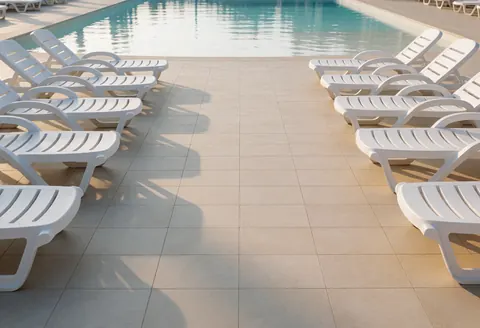 White beach chairs arranged neatly beside a clear water pool on beige tile flooring under soft morning light