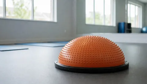 Orange bosu ball on gray floor in rehabilitation studio with blankets and mirror for balance training
